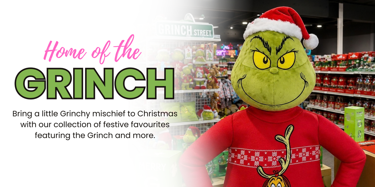 A promotional graphic for a Grinch-themed store display, featuring a large plush Grinch figure in a red Santa sweater and hat in a retail store aisle. Large text on the left reads 'Home of the GRINCH' with smaller descriptive copy below.